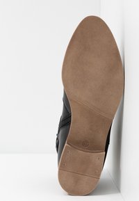 Zapato de cuero negro con parte superior lisa, cremallera lateral y suela de goma de color marrón claro con acabado texturizado. Talla marcada en la suela.