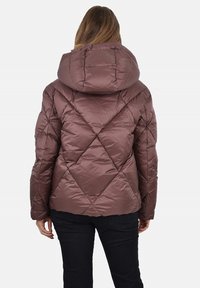 Piumino color malva con cappuccio. Presenta un motivo trapuntato a forma di diamante, polsini a costine e una vestibilità leggermente affusolata. Il materiale è lucido.