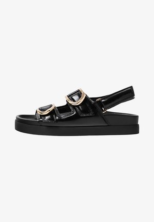 Sandali in pelle verniciata nera con tre cinturini regolabili, dotati di fibbie in tonalità oro e una spessa suola piattaforma nera.