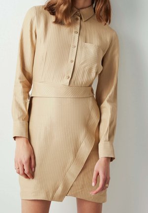 Beige striped shirt dress with a collar, buttoned front, chest pocket, and belted waist. Smooth texture and long sleeves with cuff details.