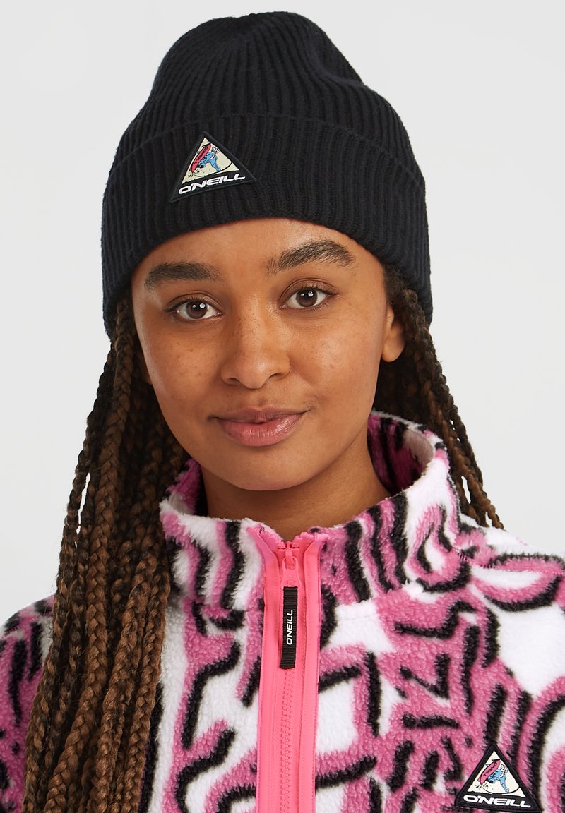 Berretto di maglia nero con un patch a forma di triangolo e una giacca in pile rosa con un motivo astratto nero e rosa. Cerniera con un cursore nero.