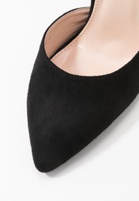 Escarpin en daim noir avec un bout pointu et un intérieur lisse de couleur claire. Présente un design sans coutures et sans éléments métalliques ni accents visibles.