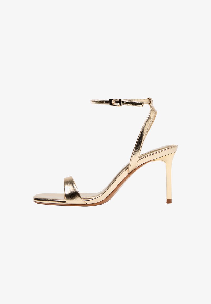 Zlatna metalik sandala s visokim potpeticama, remenom oko gležnja i kopčom, otvorenih prstiju i tankom štiklom, na bijeloj pozadini.