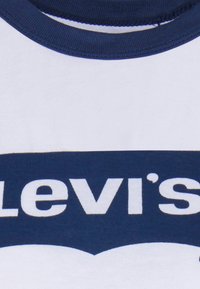 Camiseta blanca de algodón con cuello redondo azul marino y gran logo gráfico en blanco y azul marino de "Levi's" en el centro.