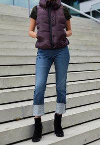 Lila pufferväst med huva, knappstängning, tillsammans med blå jeans i denim med uppvikta fållar och svarta högklackade ankle boots.