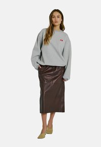 Grå oversized sweatshirt med röd logotyp, kombinerad med en brun lädermidikjol. Modell som bär ljusgula spetsiga skor.