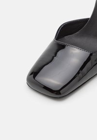 Gros plan d'une chaussure noire en cuir verni à bout carré avec une finition brillante et lisse et des bords cousus.