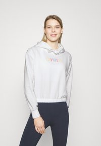 Biely flísový mikina s kapucňou a šnúrkou, ktorá má farebný logo "CHAMPION". Navrhnutá s priliehavým pásom a dlhými rukávmi.