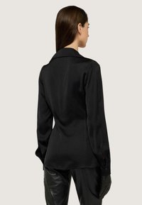 Blusa nera in satin con maniche lunghe, colletto a punta e polsini con bottoni, caratterizzata da una superficie liscia e una vestibilità sartoriale.