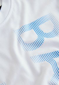 Tissu blanc avec un motif linéaire bleu formant des formes géométriques abstraites, montrant la texture et de légers plis.