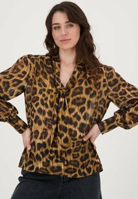 Blouse met luipaardprint van glanzende gouden en zwarte stof, met strikdetail aan de hals en lange mouwen met gathered manchetten.