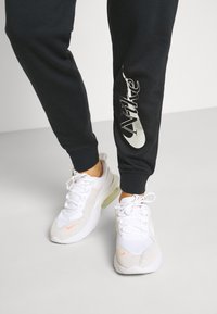 Svarta joggarbyxor med silverfärgad "Nike"-logotyp på sidan, kombinerat med vita och grå Nike-sneakers som har en tydlig luftkuddenhet.