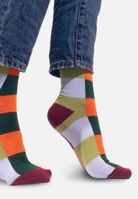 Kolorowe skarpetki z geometrycznym wzorem w odcieniach pomarańczowym, zielonym, żółtym i purpurowym z burgundowym palcem. Wykonane z miękkiego, elastycznego materiału.