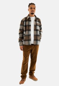 Gekruist flanellen shirt in grijs, bruin en wit, over een wit T-shirt; gecombineerd met een bruine corduroy broek en bruine sneakers.