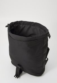 Black fabric backpack with a cylindrical shape, cinched top, and adjustable straps. Features smooth texture and minimalistic design.