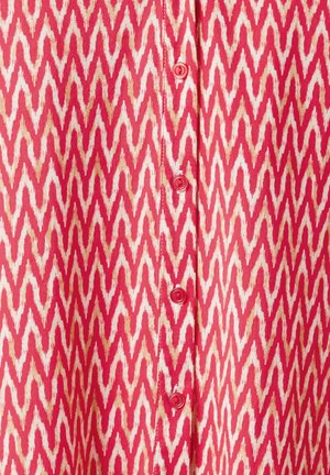 Red and cream zigzag patterned fabric with buttons down the center. The texture appears smooth and lightweight.