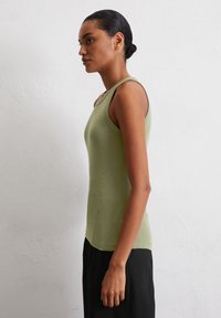 Haut ajusté sans manches en tissu côtelé vert olive clair. Texture lisse avec un décolleté arrondi, associé à un pantalon noir.