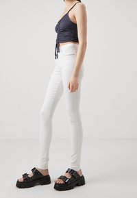 Top sin mangas azul marino con detalle fruncido, combinado con jeans pitillo blancos de cintura alta y sandalias de plataforma negras con tachuelas decorativas.