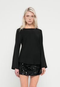 Top preto de manga comprida com decote largo, combinado com uma mini saia preta de lantejoulas. Textura lisa, silhueta ajustada e mangas flare em destaque.