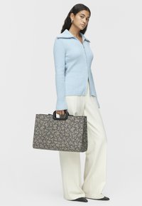 Strukturalny sweter w jasno-niebieskim kolorze z fakturą, z przodu na zamek, w połączeniu z dużą torebką o geometrycznym brązowym wzorze i czarnymi uchwytami.