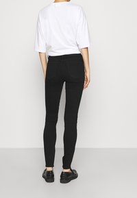 Jeans negros ajustados de talla media con cintura media y bolsillos traseros, combinados con una camiseta blanca de gran tamaño y zapatos negros. Textura de denim suave.