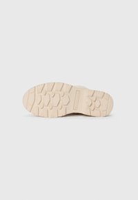 Kremfarget såle på sneakers laget av teksturert gummi, med et heksagonalt mønster og flere spor for bedre grep.