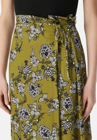 Groene bloemen wikkelrok met zwart-witte bloemenpatronen, gestrikt rond de taille met een stoffen riem, gemaakt van lichtgewicht textiel.