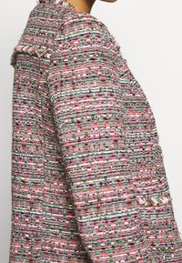 Teksturowana wełniana kurtka z wielokolorowym splotem w odcieniach różu, zieleni i bieli, z frędzlami na krawędziach i ozdobnym kołnierzem.