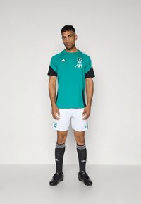 Krátký rukáv fotbalového dresu v tyrkysové a černé barvě s bílými šortkami a černými ponožkami, s klubovým logem a černými doplňky na rukávech.