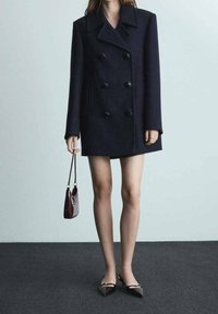 Navy kaksirivinen villakangastakki suurilla mustilla napilla, sivutaskuilla ja jämäkällä muotoilulla, yhdistettynä pieneen laukkukoteloon.