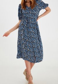 Blå blommig midiklänning med puffärmar, åtsittande midja och flödande kjol. Tyget har små blommor på en svart bakgrund.