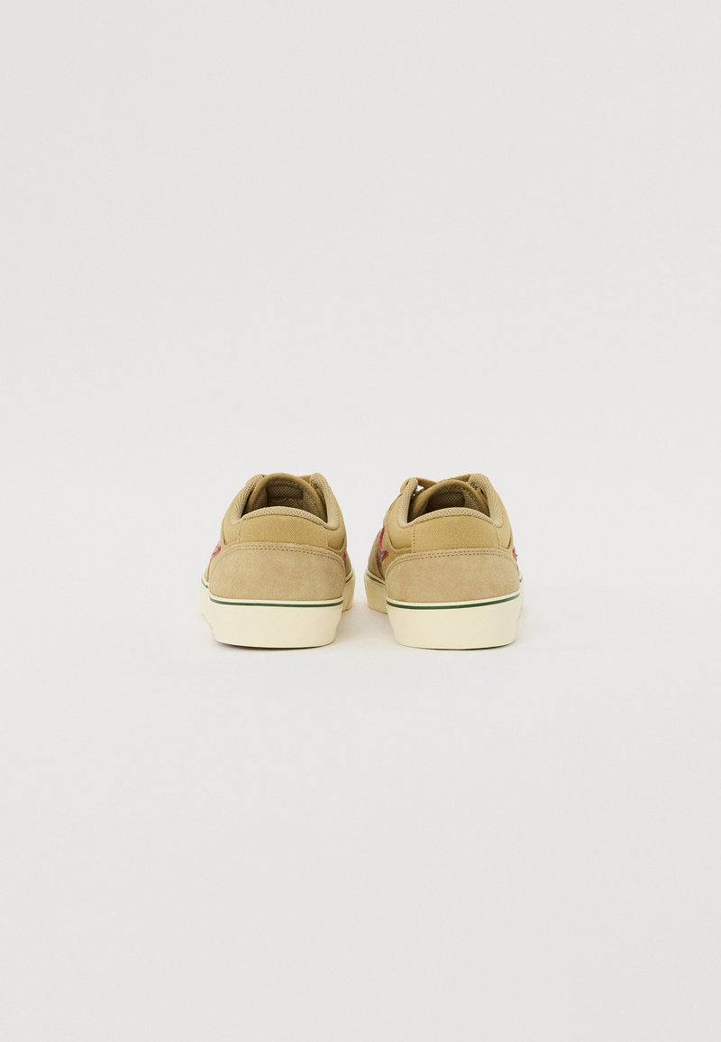 Zapatillas de gamuza en tono beige con acabado texturizado, que cuentan con un logotipo rojo en contraste, suelas de goma blancas y un collar acolchado para mayor comodidad.