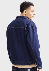 Dunkelblaue Jeansjacke mit lockerer Passform, mit Knopfverschluss, Vordertaschen und kontrastierenden Nähten. Gerippter Saum und Bündchen.