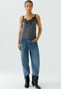 Graues Top mit schwarzem Spitzenbesatz, kombiniert mit lockeren blauen Jeans mit aufgesetzten Taschen. Das Model trägt schwarze High Heels. Einfacher, lässiger Look.