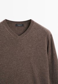 Bruine v-hals trui gemaakt van zacht breimateriaal. Beschikt over een ribbelhals en -zoom, met een gladde textuur en minimale details. Merkkenlabel zichtbaar.