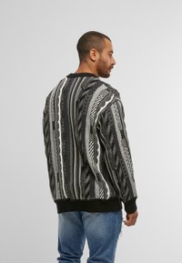Schwarzer und weißer gemusterter Pullover mit Rundhalsausschnitt, der strukturierte Designs, lange Ärmel und einen gerippten Saum aufweist.