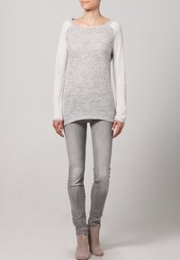 Světle šedý pletený svetr s kontrastními bílými rukávy, kulatým výstřihem a dlouhými rukávy, doplněný o slim fit šedé džíny a kotníkové boty.