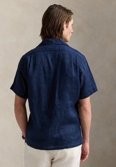 Rövid ujjú, tengerészkék lenvászon ing klasszikus gallérral és texturált felülettel. Laza szabású, finom varrási részletekkel. Hátsó nézet.