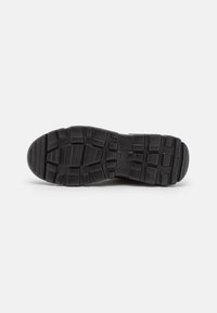 Semelle de chaussure en caoutchouc noir avec des motifs de bande de roulement rectangulaires et carrés profonds, présentée sur un fond clair.