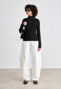 Black long-sleeve turtleneck top, white wide-leg trousers, and black shoes. The outfit includes a shiny black shoulder bag and sunglasses.