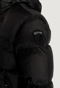 Giubbotto piumino nero con finitura lucida, dotato di una toppa con logo sulla spalla, gomiti a costine e un design compatto e trapuntato.