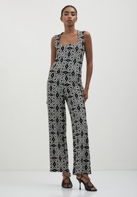 Jumpsuit a righe nero e bianco con scollo quadrato, gamba larga e design geometrici, realizzato in un tessuto morbido.