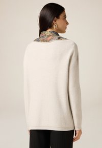 Hellgrauer Pullover mit lässigem Schnitt, der ein kunstvolles florales Muster am Kragen aufweist. Weicher Griff und dezente Glanzdetails.