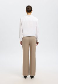 Hvit bluse med lange ermer, knappemansjetter og rett snitt, kombinert med høytlivede, beige bukser og svarte spisse hæler.