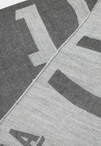 Tessuto grigio e grigio chiaro con una texture liscia, caratterizzato da audaci lettere nere astratte e cuciture visibili lungo la cucitura.