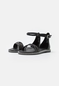Black leather sandals with ankle strap, open toe design, and decorative white stitching along the sole. Flat heel for comfort.
