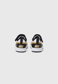 Crno-bijeli tenisice s zlatnim Nike logotipom, s glatkom kožnom završnom obradom i sigurnom trakom straga. Ravni gumeni potplat.