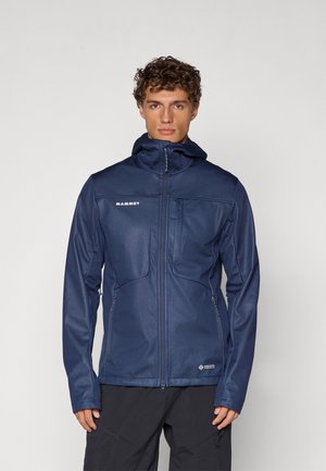 Navy blue softshell jacket with a zip front, two chest pockets, and a hood. Features textured fabric and a slim fit design.