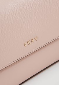 Růžová kožená kabelka s texturovaným povrchem, zlatým logem "DKNY" a odpovídajícím prošíváním podél okrajů. Kompaktní obdélníkový tvar.