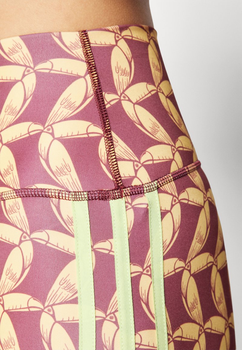 Leggings a vita alta con un motivo bordeaux e giallo, dotati di strisce laterali verdi lime a contrasto e dettagli di cucitura visibili.